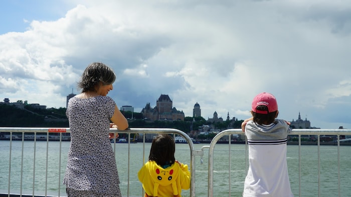Une mère et ses deux enfants accoudés à une barrière métallique. Ils regardent le fleuve et Québec.