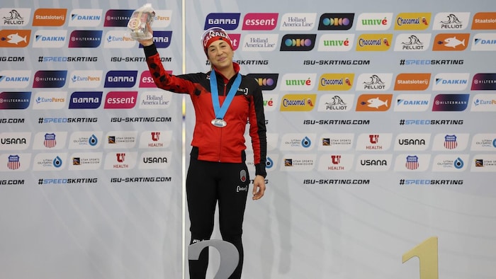 Debout derrière un grand numéro 2 argenté, elle brandit une médaille en souriant.