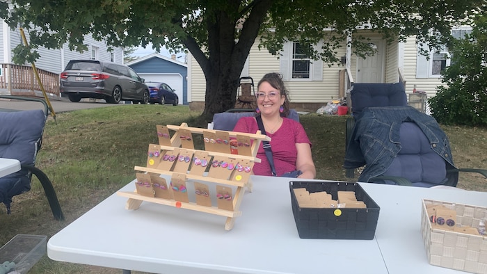 Une vendeuse d'artisanat souriante devant une maison. 