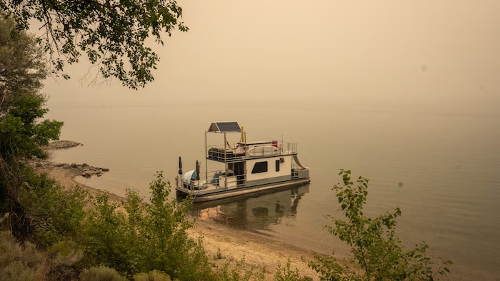 Un épais nuage de fumée enveloppe un lac où un bateau est à l’arrêt.