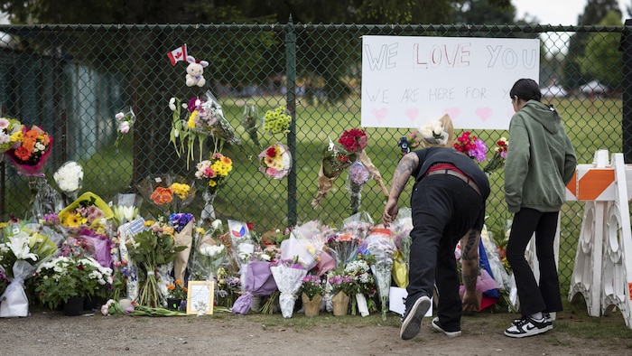 Un tas de bouquet de fleurs le long d'une clôture, sur les lieux d'un drame à Vancouver. Des personnes en ajoutent un, le 27 avril 2025.
