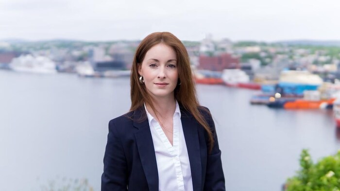 Une femme habillée en tenue de bureau, debout devant une photo d'un port de pêche flou.