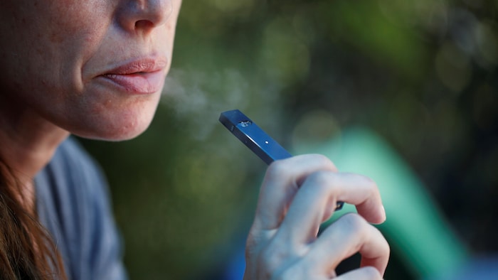 Une femme fume une cigarette électronique.