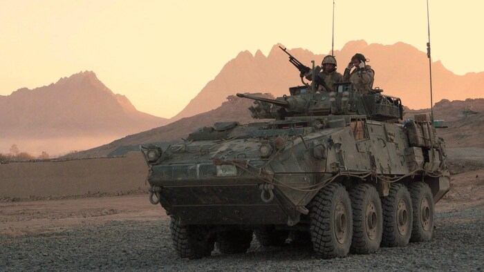 Deux membres des Forces armées canadiennes à bord d'un véhicule d'assaut LAV dans un paysage aride.