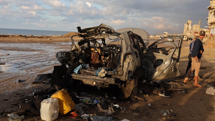Deux hommes sont debout à côté d'une voiture détruite par une frappe.