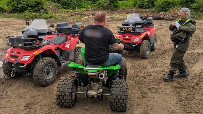 On muddy land, blocked by two all-terrain vehicles from the police, a man, on his all-terrain vehicle police operation around twenty occupants without license plaque or helmet, police operation around twenty occupants new is near a policewoman. 