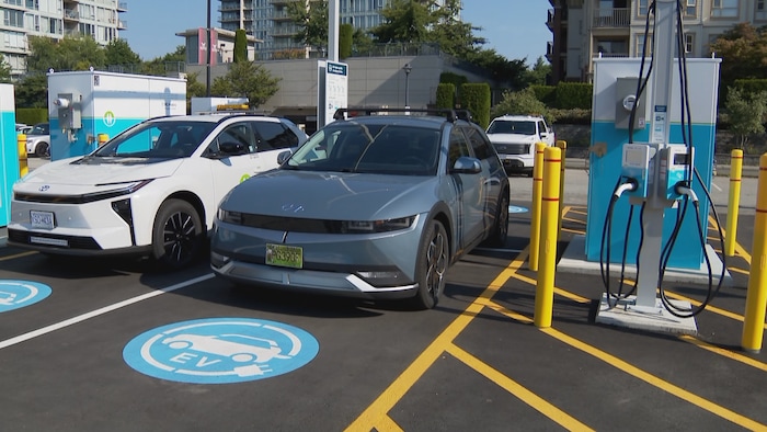 Une voiture blanche et une grise garées dans des places réservées avec des stencils « EV » bleus, connectées à des bornes BC Hydro blanches et bleues.