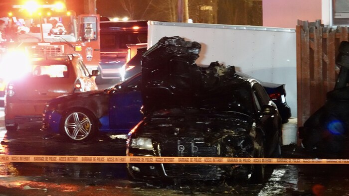 Des véhicules incendiés dans un stationnement, la nuit, derrière un ruban de police orange délimitant la scène de crime.