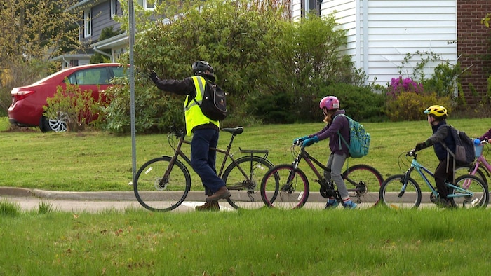 Un adulte à vélo avec veste réfléchissante, deux élèves derrnière lui.