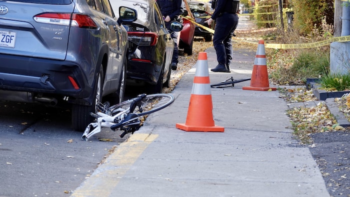 Un vélo coupé en deux se trouve par terre à côté d'un trottoir, sa deuxième roue est un peu plus loin.