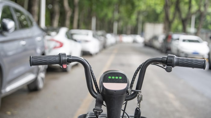 Un vélo électrique dans une rue étroite bordée de voitures stationnées des deux côtés.