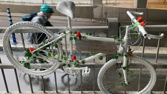 Un vélo sur lequel des fleurs artificielles ont été installées est accroché sur une clôture en métal, sous le viaduc.
