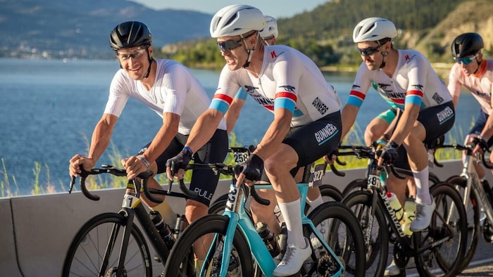 Un groupe de cyclistes vêtus de blanc roule devant un lac. 