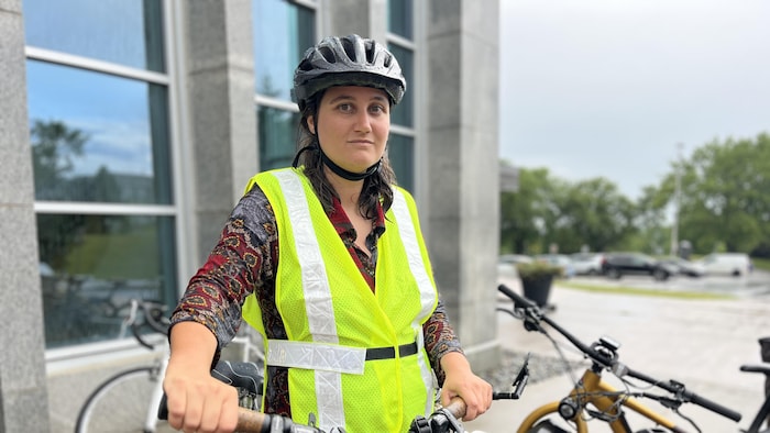 Ariane Lafontaine tient son vélo. Elle porte un casque et un dossard de sécurité.