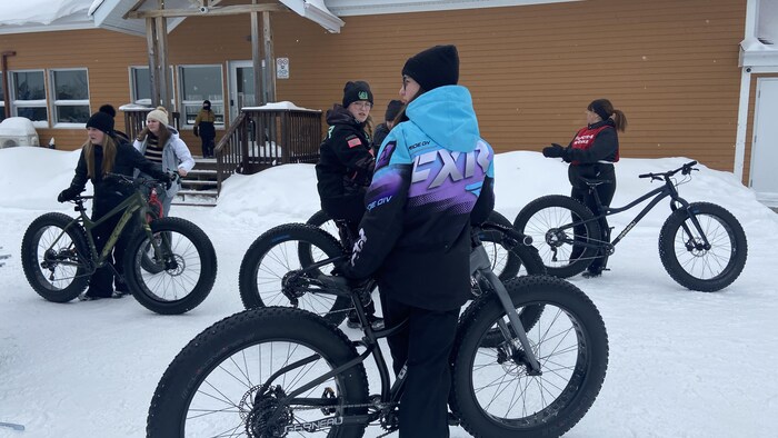 Plusieurs personnes debout à côté de vélos à pneus surdimensionnés dans une cour enneigée.