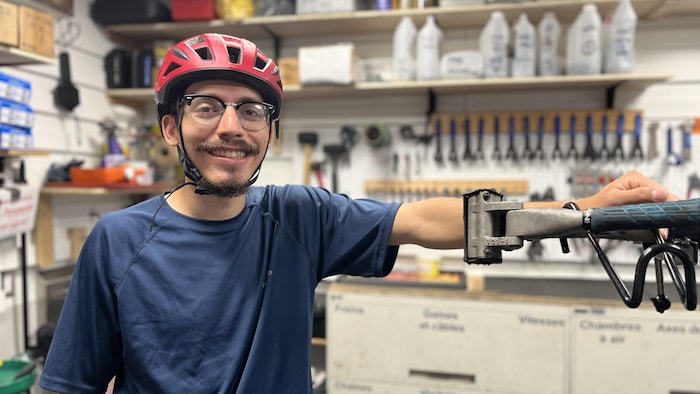 Roberto Arturo Gonzalez Godinez se trouve dans l'atelier vélo de la coopérative La Déraille. Il porte son casque de vélo. Derrière lui se trouvent plusieurs outils accrochés au mur.