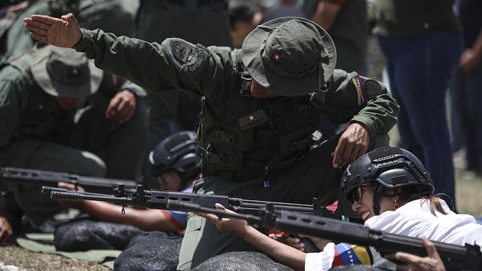 Un instructeur pointe où tirer à une personne en formation avec un fusil entre les mains.