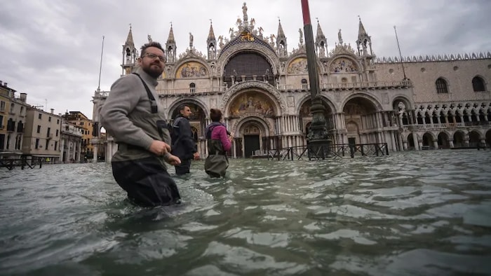 Trois personnes se tiennent sur la place Saint-Marc, et elles ont de l'eau jusqu'aux genoux.
