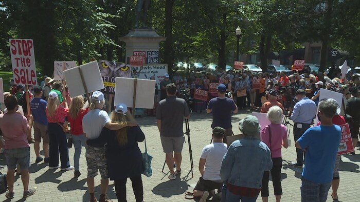 Un groupe de personnes tenant des pancartes sont rassemblées dans un espace public extérieur.