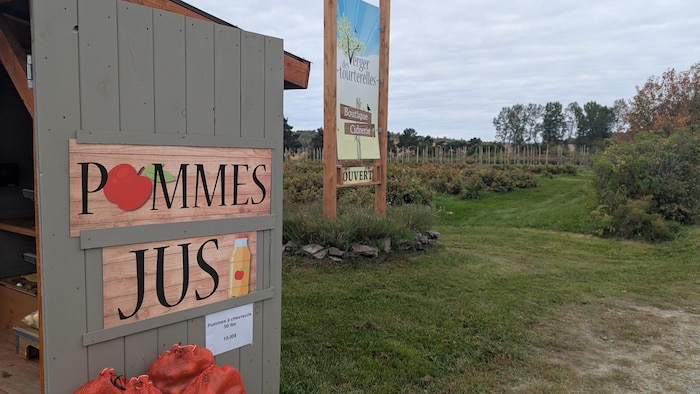 Une grosse affiche écrit « pommes et jus », en plus de la pancarte de bienvenue du verger.