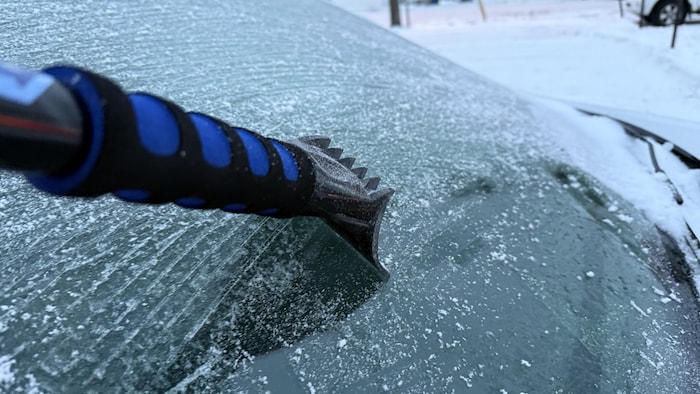 Un grattoir est utilisé pour enlever le verglas sur la pare-brise d'une voiture.