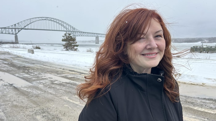 Une femme souriante devant un grand pont en acier.