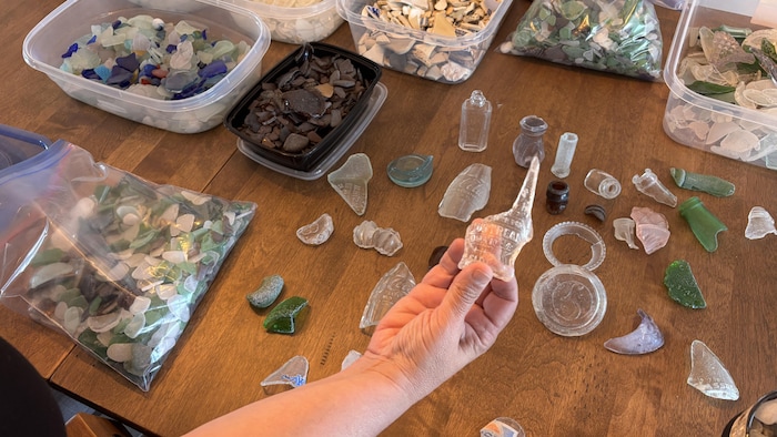 Vue de dessus d'une table en bois couverte d'une vaste collection de verre de mer, de morceaux de céramique et de vieux objets en verre.