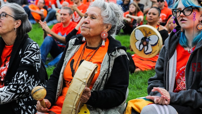 Une dame portant de l'orange tient un tambour.
