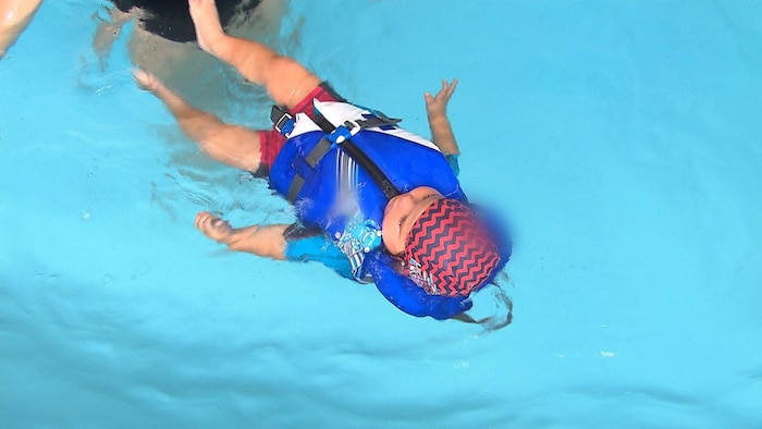 Un bébé flottant dans une piscine à l'aide d'une veste de flottaison.