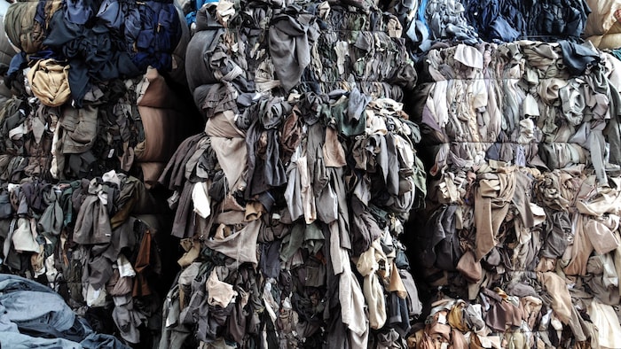 Des piles de vêtements de couleur grise sont dans un entrepôt.