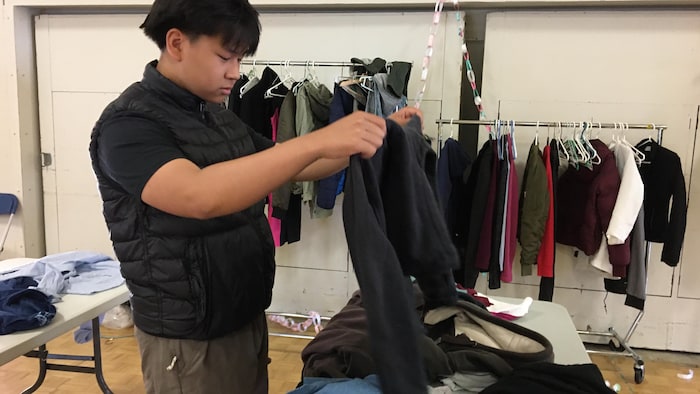 Un adolescent regarde un chandail, lors d'un événement où des vêtements d'occasion sont offerts à la communauté.