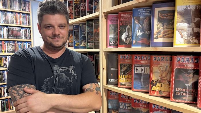 Stéphane Suprenant pose dans son sous-sol, devant sa collection de VHS.
