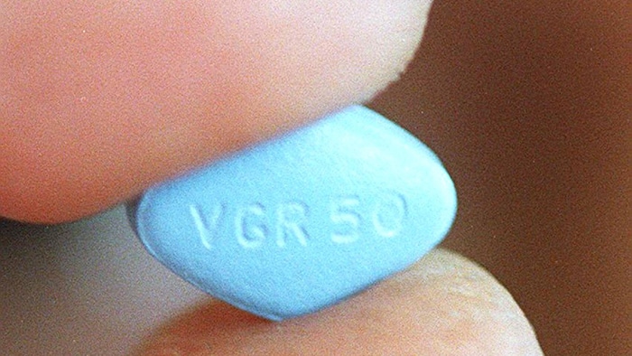 Une pilule de Viagra entre les doigts d'un homme.