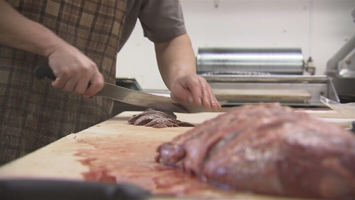 Un employé de la boucherie Côte à Côte, à Cap-aux-Meules, prépare de la viande de phoque