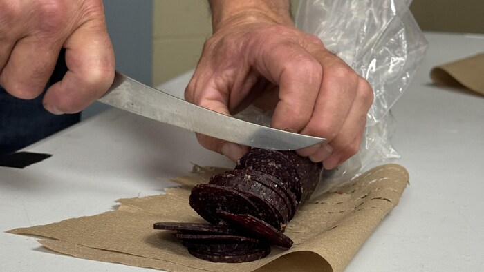 Un homme coupe des tranches de saucisson de loup marin. 