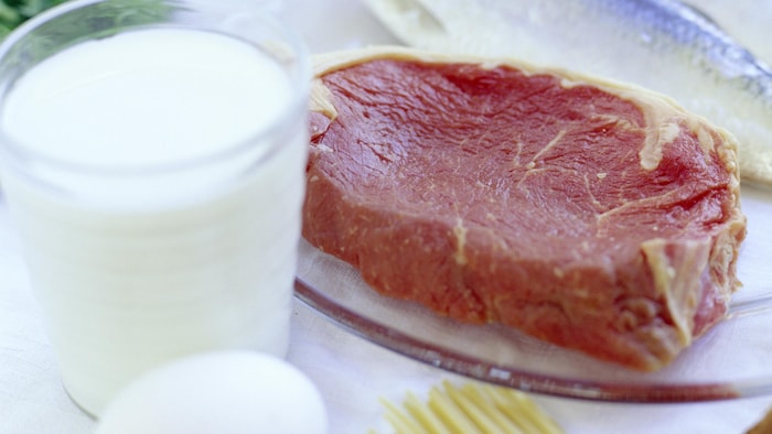 Un verre de lait est posé à côté d'une assiette contenant un morceau de viande crue.