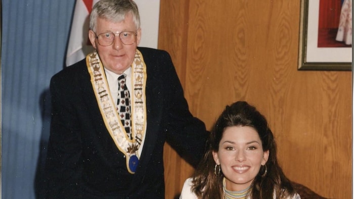 Vic Power et Shania Twain prennent la pose derrière un bureau.