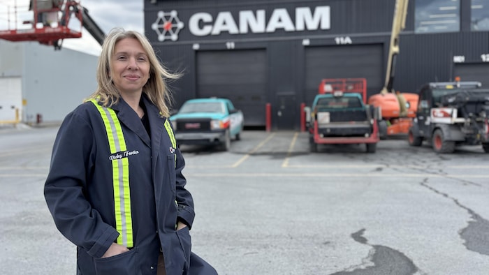 Une employée d'une entreprise de métallurgie posant devant une usine du Groupe Canam.