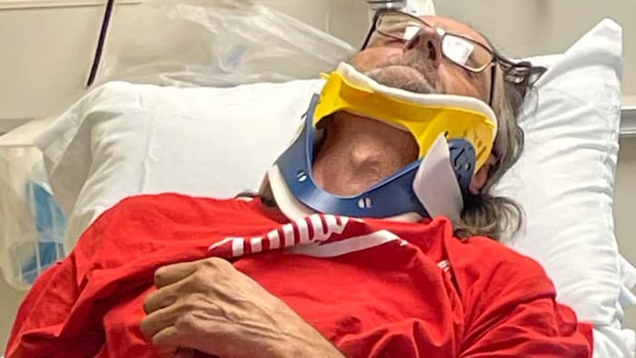 Robert Belley allongé sur un lit d’hôpital avec une minerve ou collier cervical et incapable de bouger. 