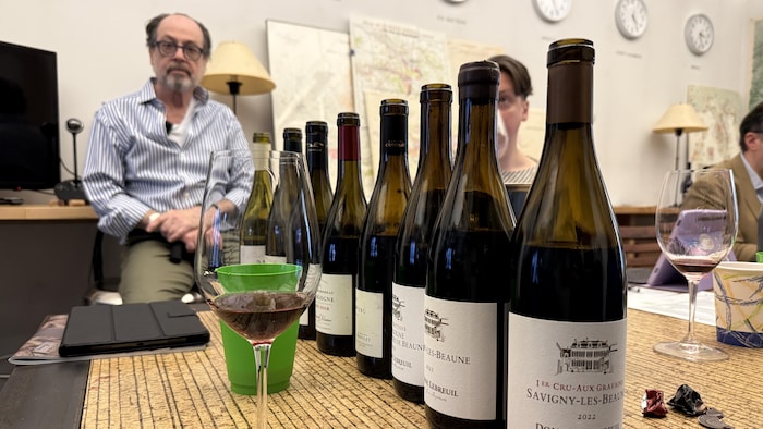 Un homme en arrière-plan de bouteilles de vin sur une table, pendant une séance de dégustation.