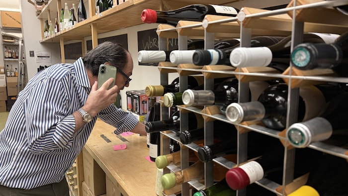 Un homme d'affaire parle au téléphone et cherche une bouteille de vin. 