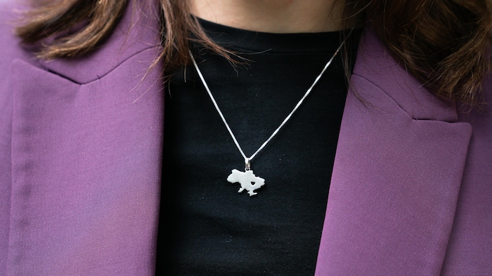 On voit la chaînette et le pendentif qui a la forme de l'Ukraine au cou de Viktoriia.