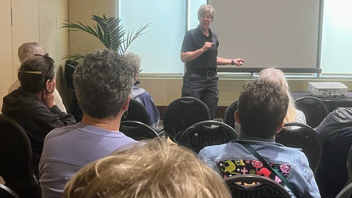 Une conférencière s'adresse à un groupe de personnes assises dans une salle de réunion.  
