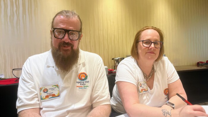 Shawn Barrie et Kate Kelly sont assis derrière une table recouverte d'une nappe blanche.  