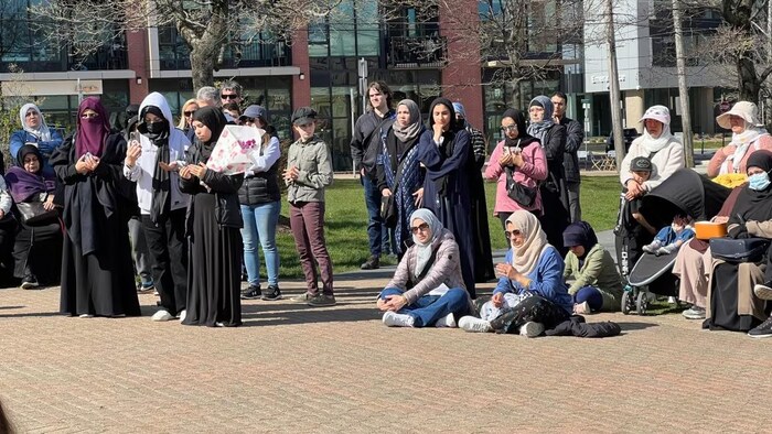 Une trentaine de personnes de la communauté musulmane écoutent un discours en tenant des fleurs