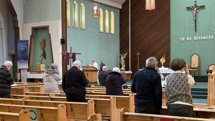 Des personnes debout dans une église font le signe de croix.