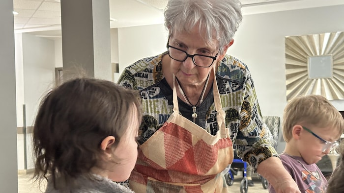 Une vieille dame tenant un bol de macaronis regarde un jeune enfant.
