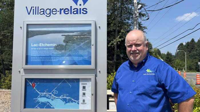 Patrick Lachance à côté d'un panneau où il est écrit «village-relais».