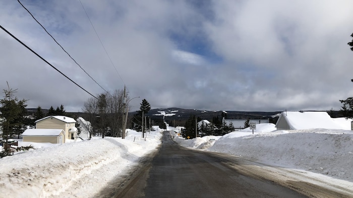Route enneigée avec maisons qui bordent la route et montagnes au loin.