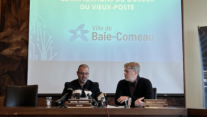 Le maire et le directeur général sont assis derrière des micros pour faire une annonce lors d'une conférence de presse.